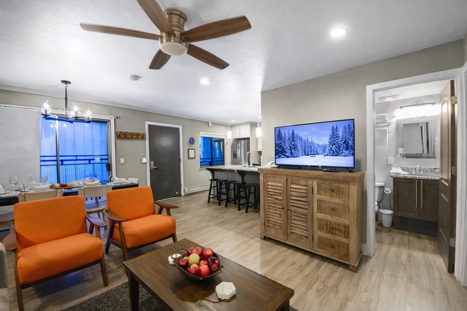 Bright, modern living area with cozy seating, snowy-scene smart TV, and a fully equipped kitchen. Warm wood accents and open layout create the perfect space to relax après-ski. Ideal for families and groups visiting Park City.