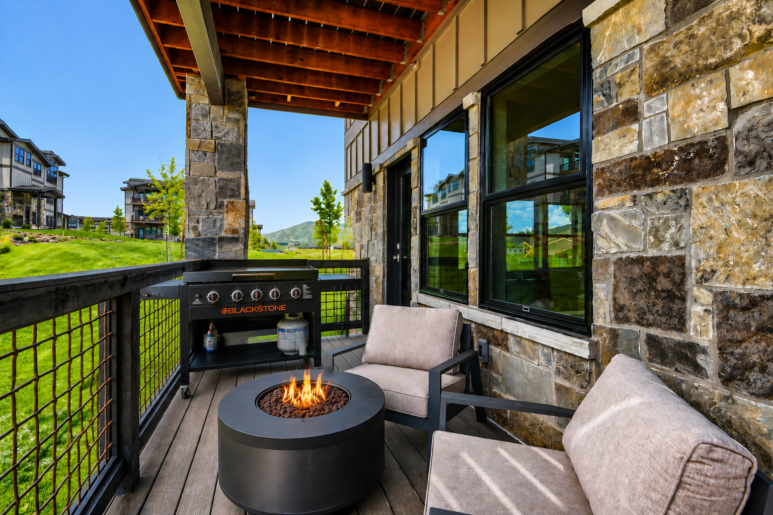 Your private covered patio with plush seating around a modern fire pit and gas grill, surrounded by mountain views and lush greens—perfect for cozy evenings.