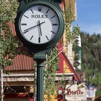 A charming clock marks the entrance to the property, set against a backdrop of mountain scenery and clear blue skies—an inviting arrival point that blends village character with alpine surroundings.