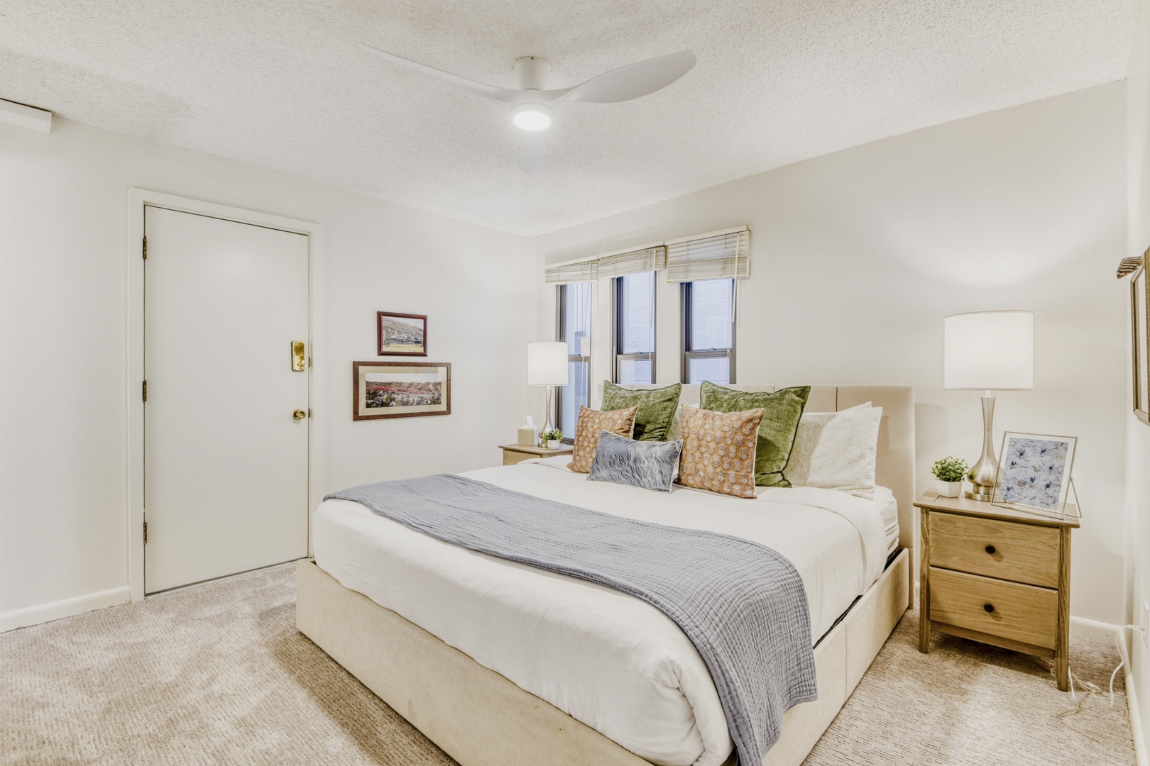 Sink into plush white bedding with colorful accent pillows in your serene bedroom, featuring natural light and a gentle ceiling fan breeze.