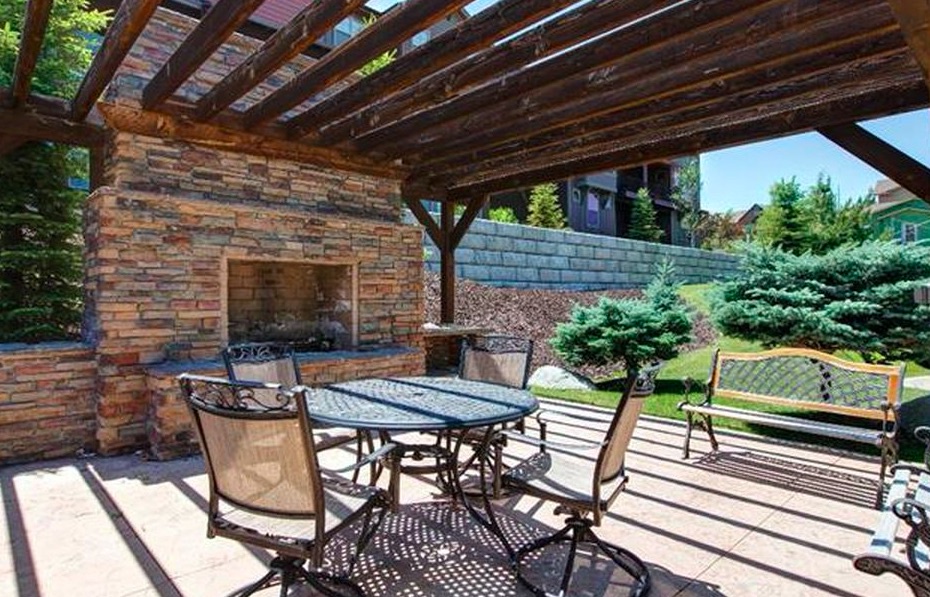 Your private outdoor retreat features a covered patio with an outdoor fireplace, perfect for relaxing evenings under the stars. Gather around the dining table or unwind on the bench, surrounded by lush gardens and a peaceful, well-maintained lawn.