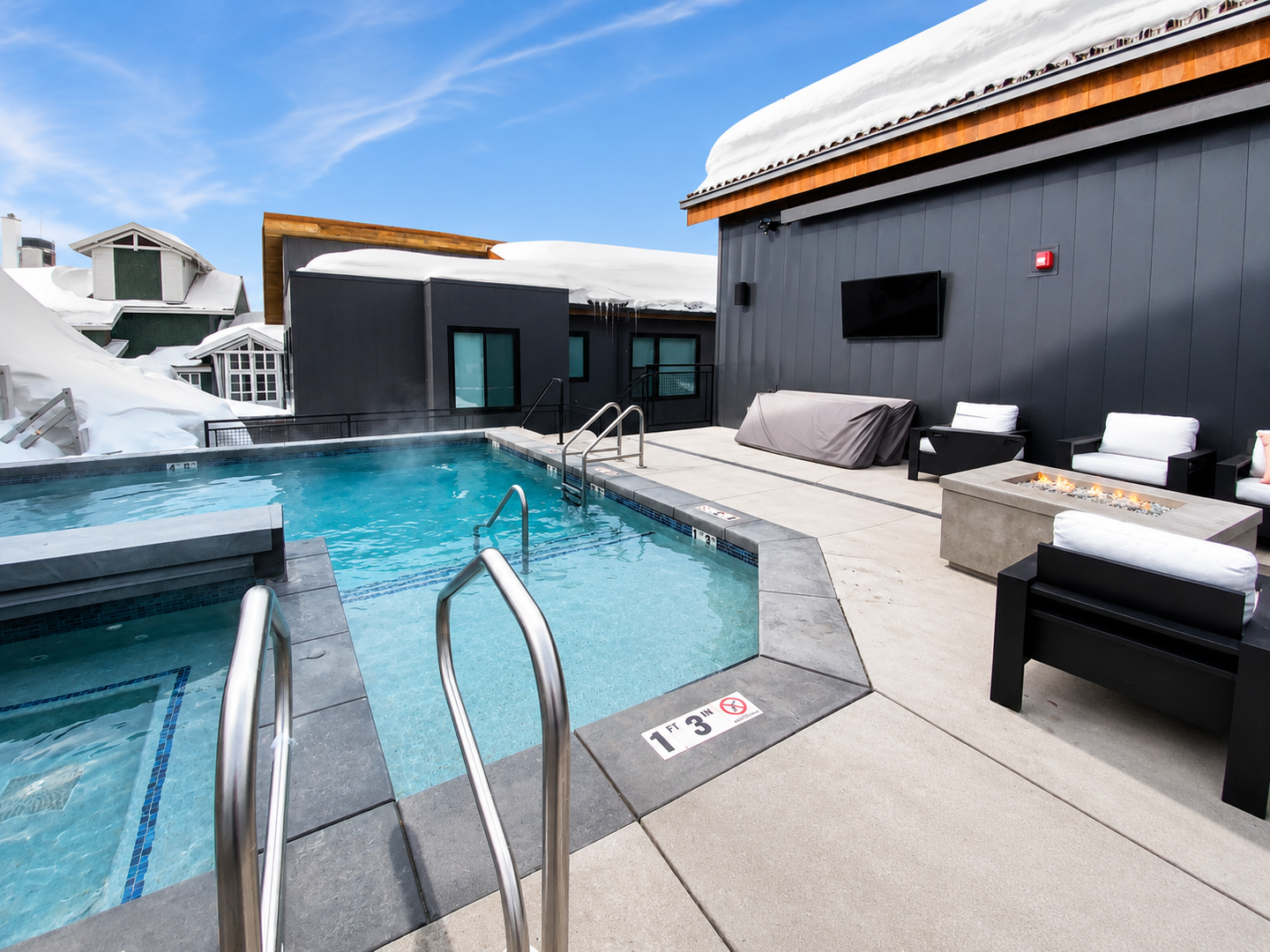 Heated outdoor pool and fire pit lounge area with mountain views, blanketed in fresh winter snow.