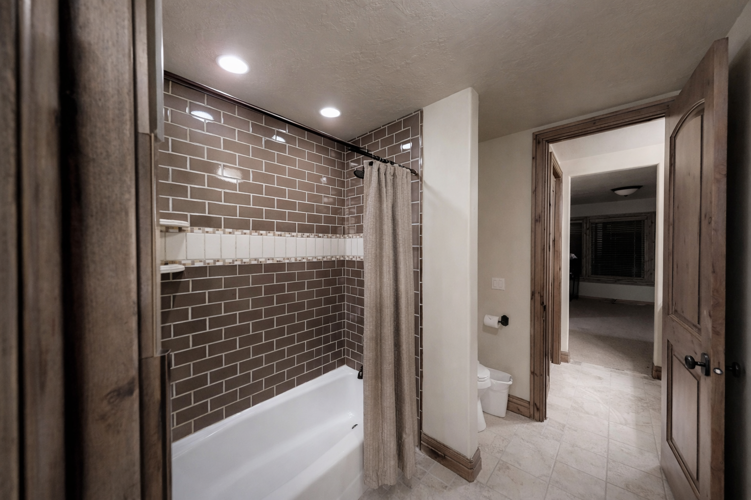 This modern bathroom features a clean white tub surrounded by stylish dark subway tile and warm recessed lighting. The spacious, bright layout ensures a comfortable and refreshing start to your day.