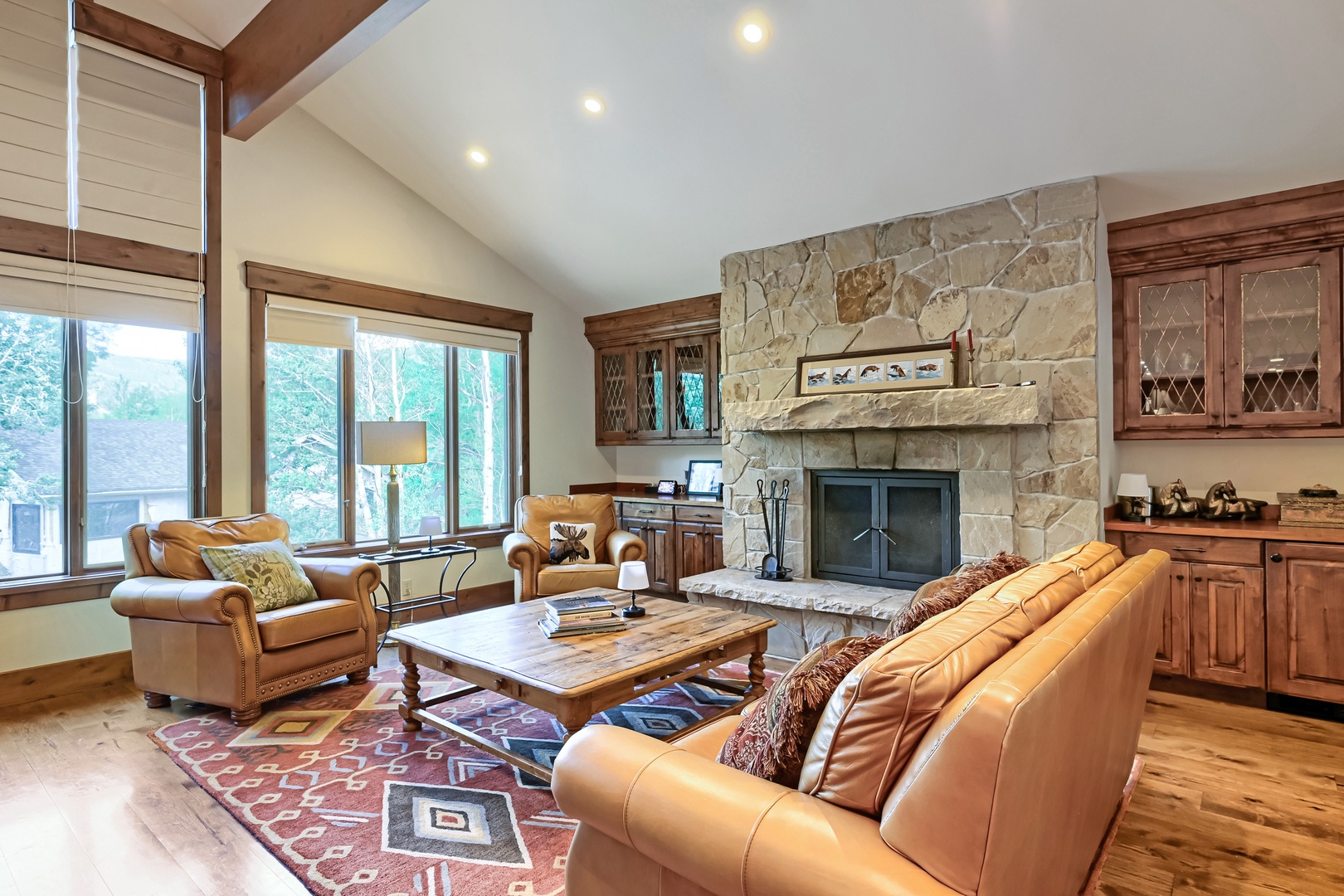 Sink into buttery leather sofas in your vaulted living room, where a stunning stone fireplace anchors the space and tall windows frame views of the surrounding pines.
