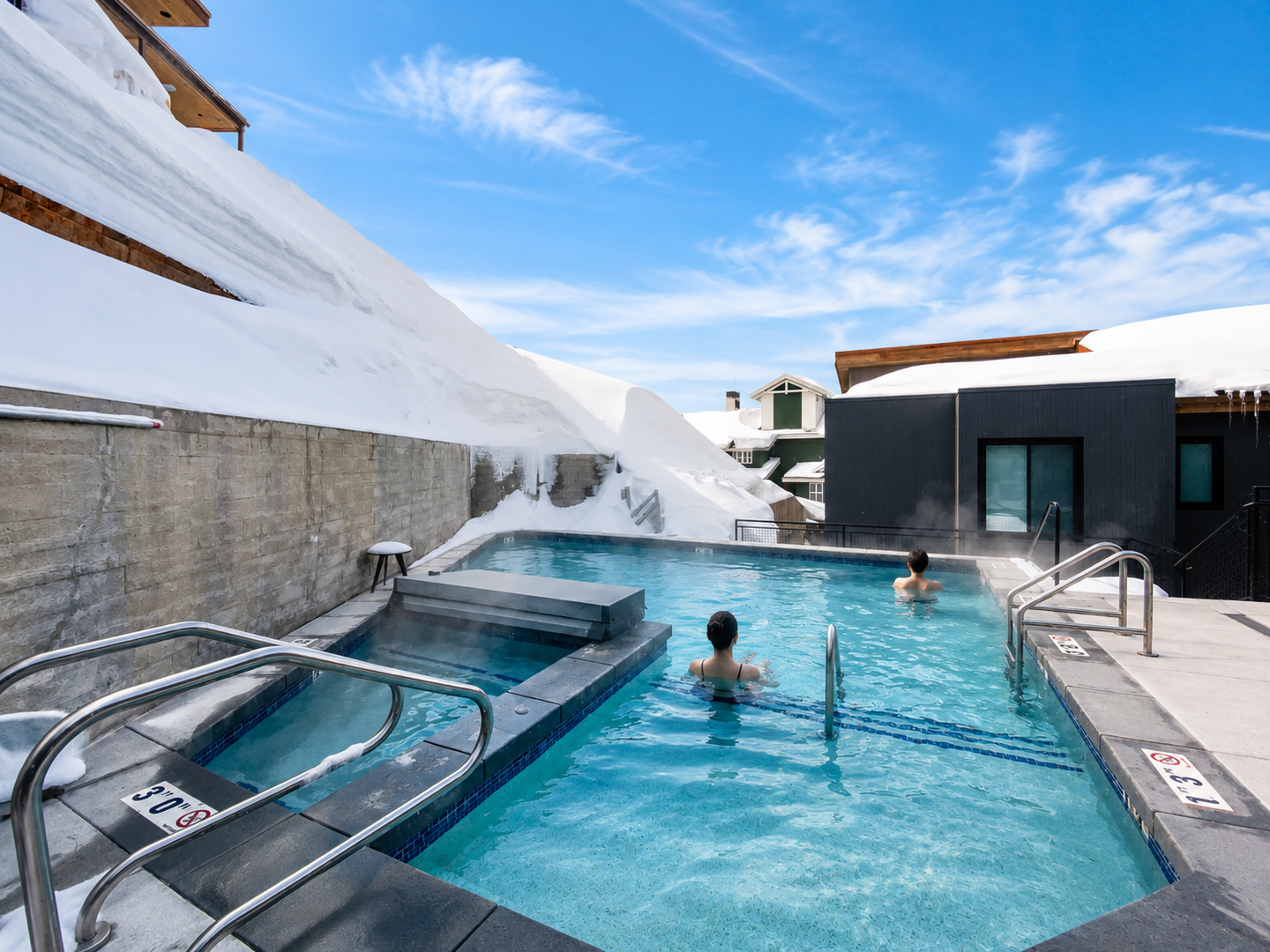 An outdoor heated pool framed by snow-capped rooftops, offering a serene alpine escape under clear winter skies.