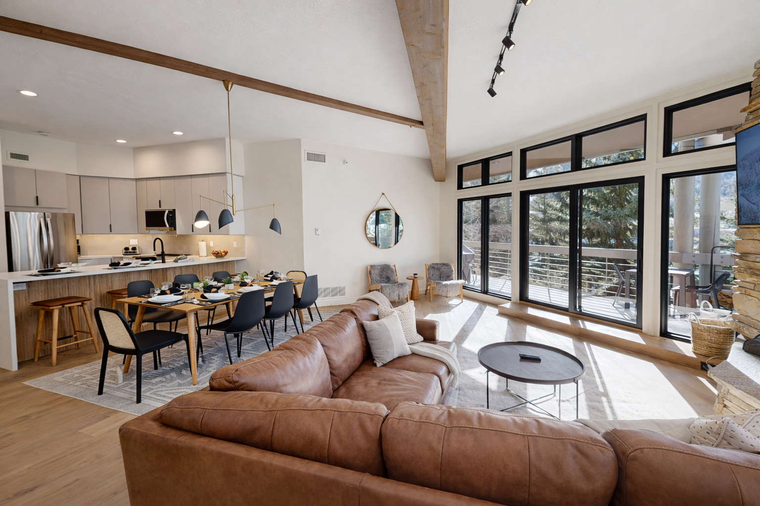 Sink into the warm leather sofa and feel the sunlight streaming through floor-to-ceiling windows as exposed beams create cozy charm above.