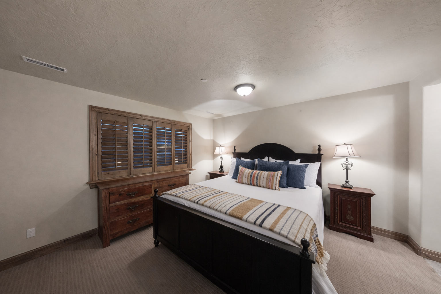 This spacious guest room features a grand four-poster bed, premium linens, and warm bedside lighting. Shuttered windows and plush carpeting create a quiet, comfortable retreat for a restful night.