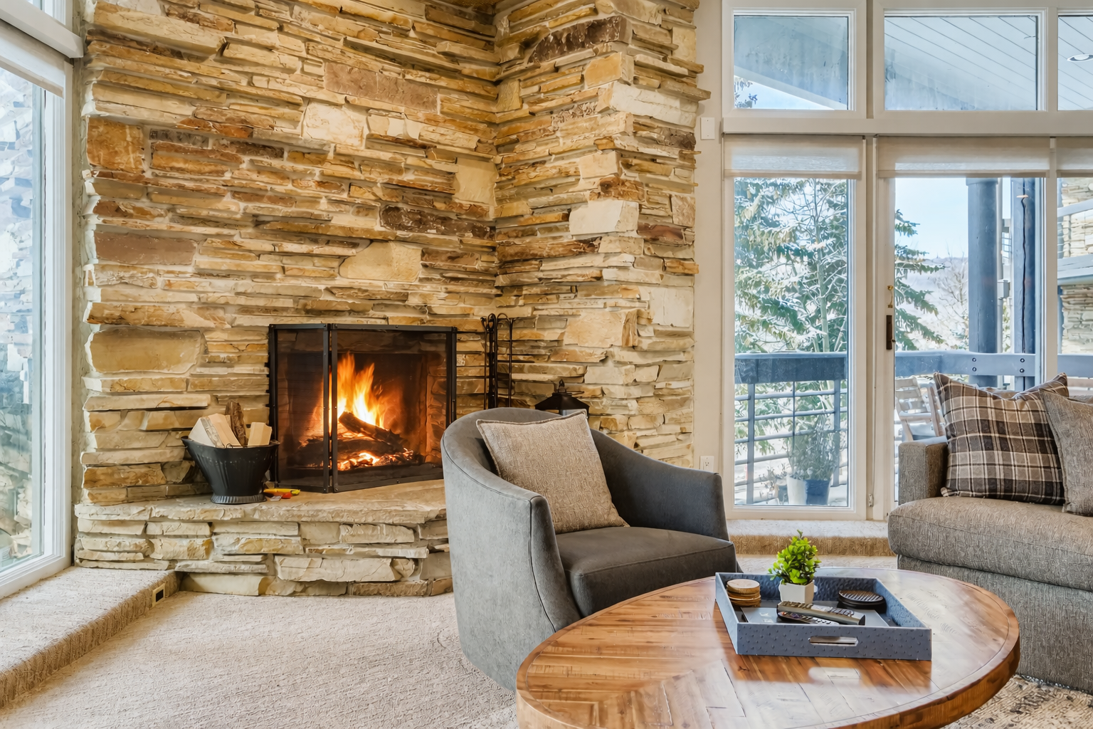Unwind in your cozy living room featuring exposed beams, stone fireplace, and large windows that frame peaceful mountain views - the perfect retreat after a day of adventure.