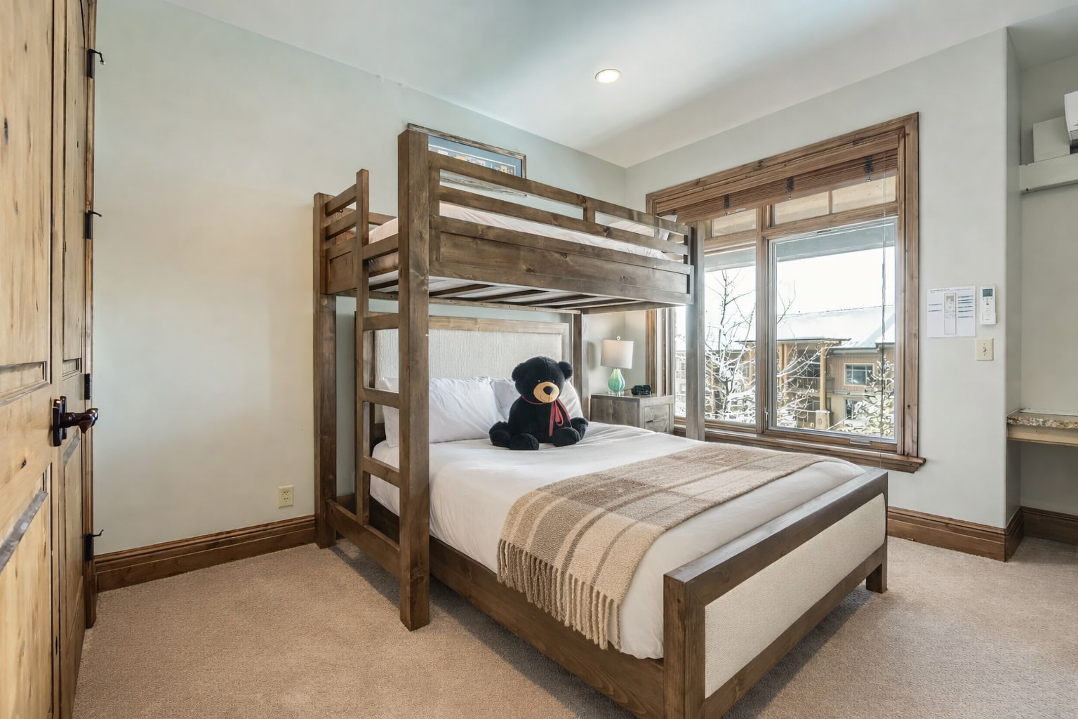This versatile guest bedroom features a twin-over-queen bunk bed, perfect for families. Highlights include a dedicated workspace, large flat-screen TV, and ample storage, all in a bright, modern mountain setting.