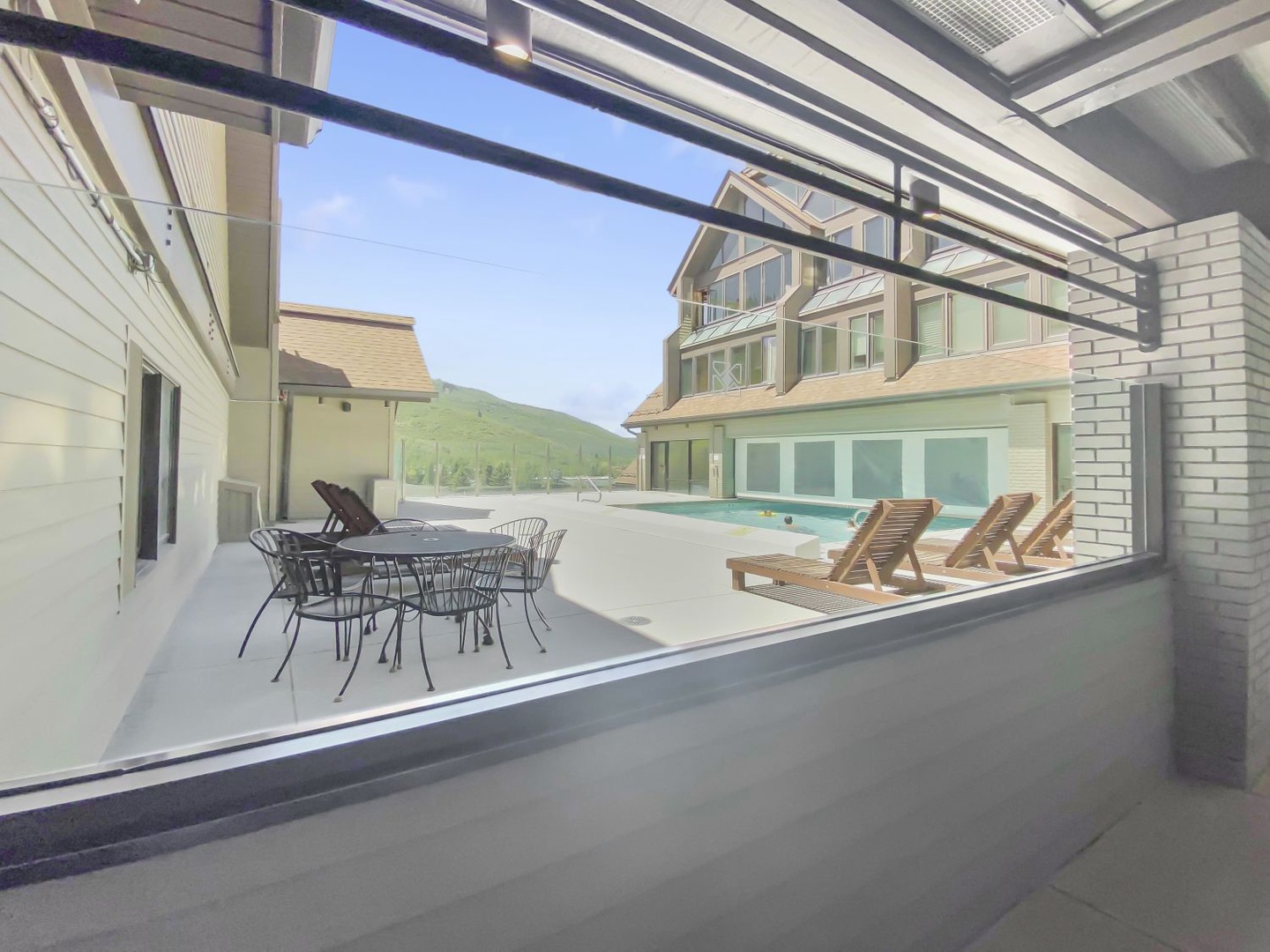 The covered patio features outdoor dining and opens to a shared pool area, with mountain scenery forming the property's scenic backdrop.