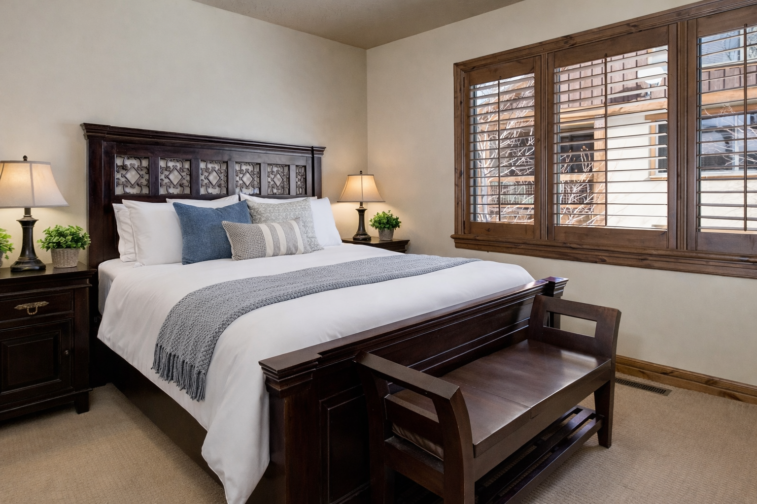 Unwind in this serene primary suite featuring a plush king bed, rich dark wood furnishings, and warm lighting. Large shuttered windows and soft neutral tones create a peaceful mountain sanctuary.
