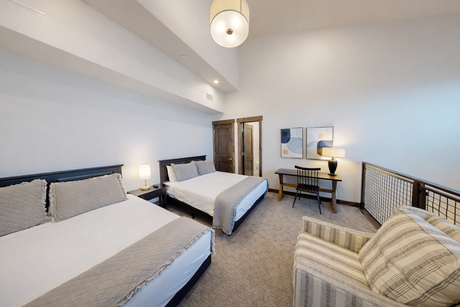 Relax in this bright and spacious bedroom featuring two plush queen beds, vaulted ceilings, and an integrated workspace. This versatile retreat offers a cozy armchair and modern art accents, perfect for families or groups.