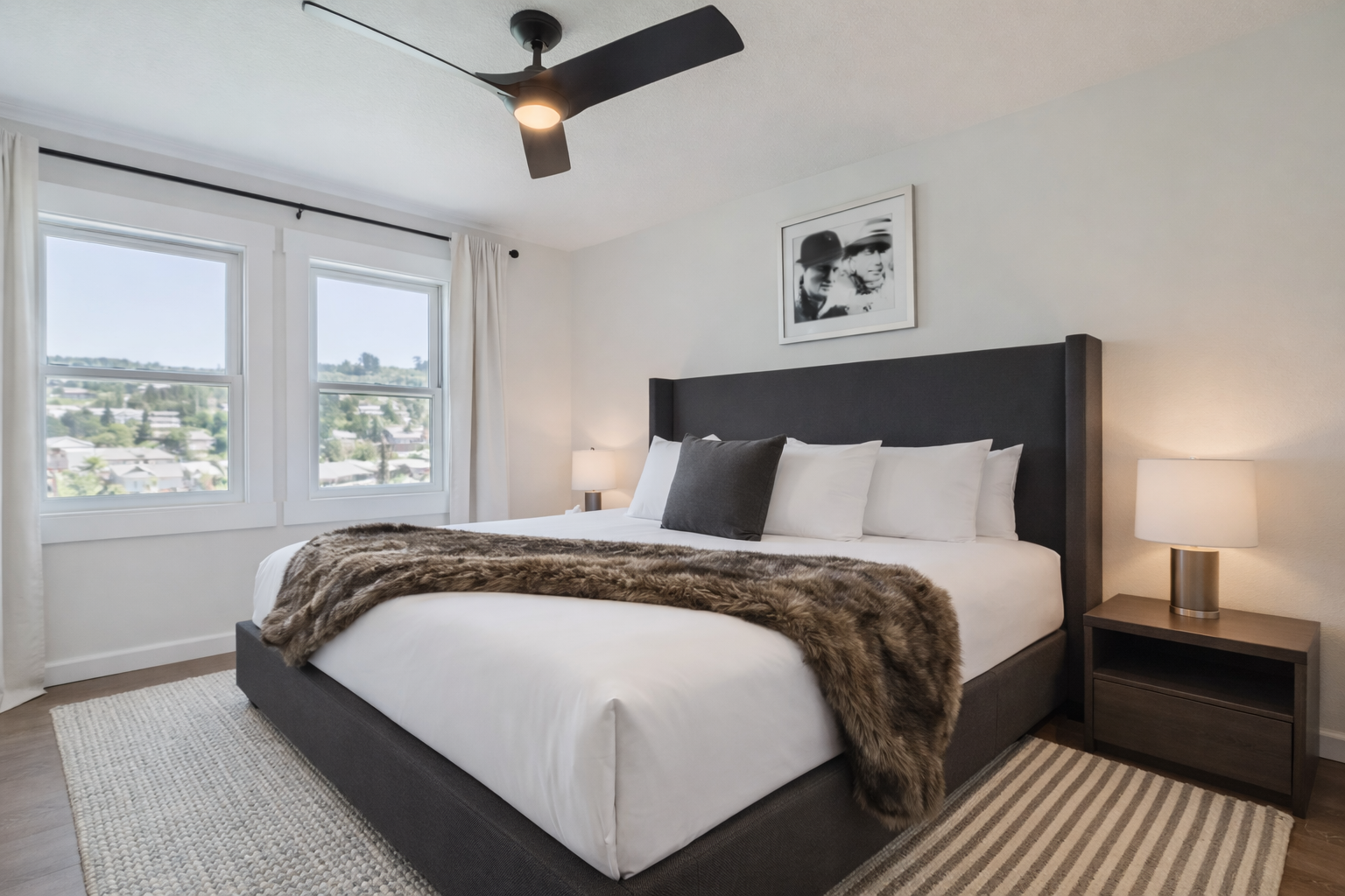 Modern & serene king bedroom with a plush bed, ceiling fan, and large windows. A tranquil space for restful sleep during your getaway.