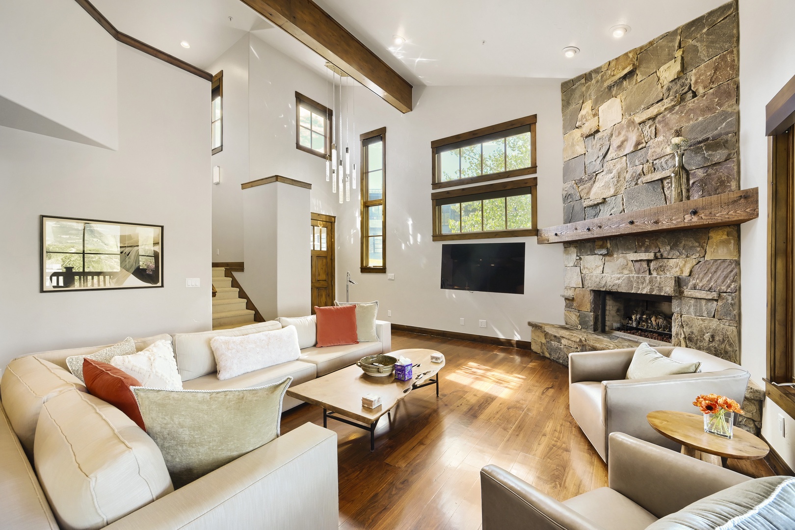 Unwind in this sunlit living room featuring vaulted ceilings, rustic timber beams, and a striking stone fireplace—your perfect retreat after a day of adventure.