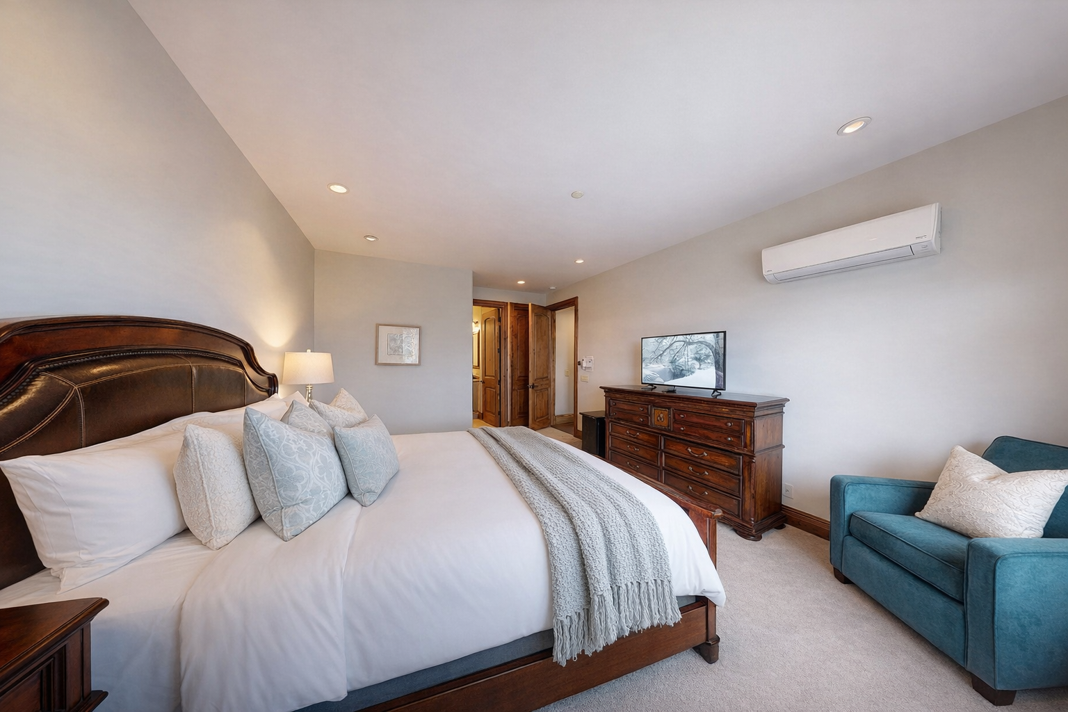 This spacious master suite features a luxurious king bed, soft linens, and a large dresser with a smart TV. Recessed lighting and neutral tones create a bright, tranquil retreat.