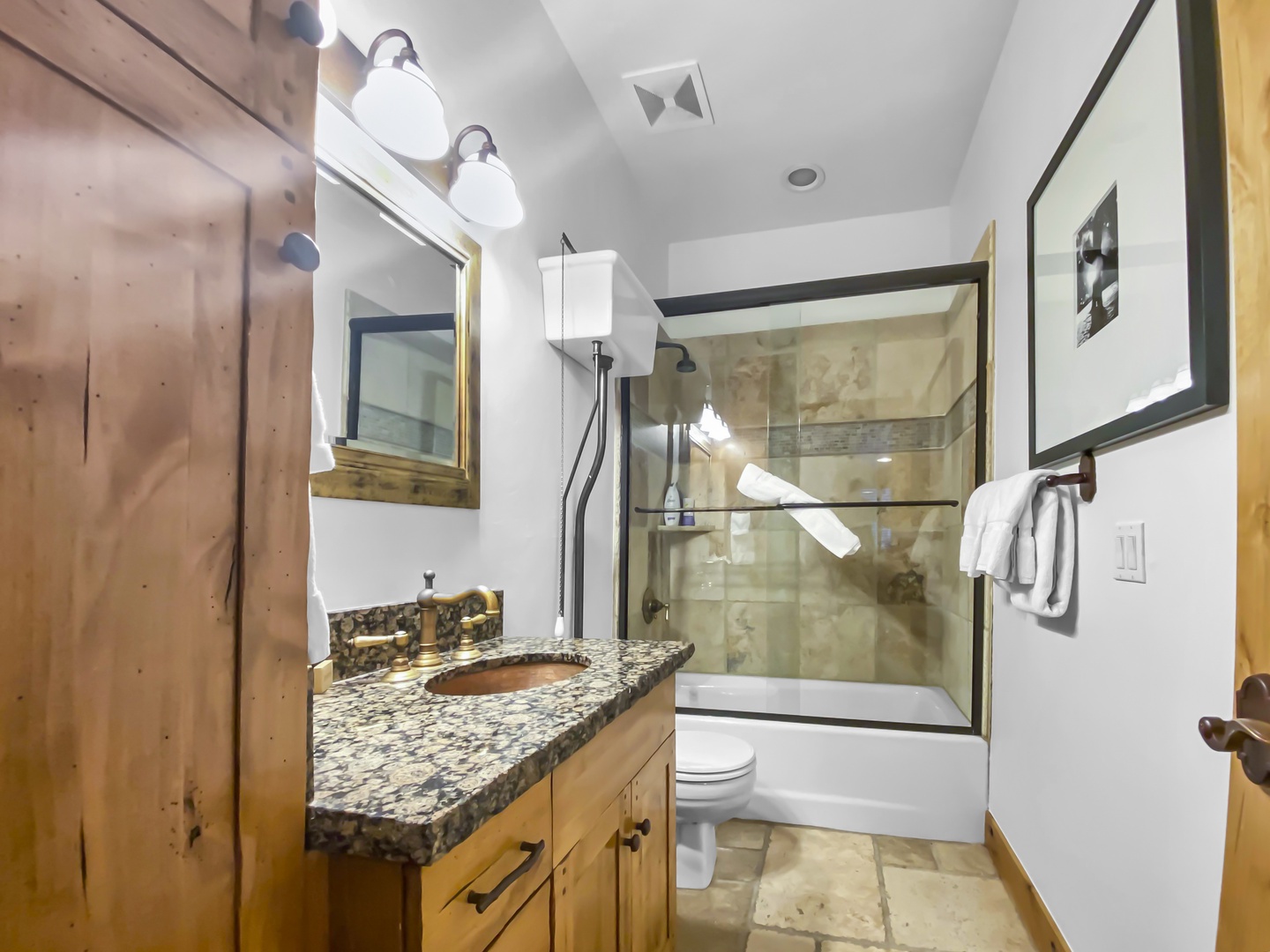 Indulge in this inviting bathroom featuring a rustic wood vanity with a stylish copper sink set in a granite countertop. A tub/shower combo with a sleek glass enclosure completes the serene, natural aesthetic. Unit B