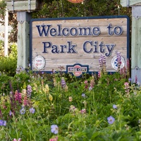 A welcoming entrance sign to Park City, surrounded by vibrant purple wildflowers and lush greenery, marks your arrival to this charming mountain destination.
