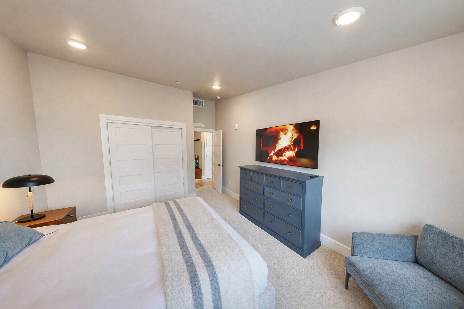 Stay in this serene, modern bedroom featuring a plush king-sized bed with a stylish channeled headboard. Large windows flood the space with light, while a cozy armchair offers the perfect spot to unwind.