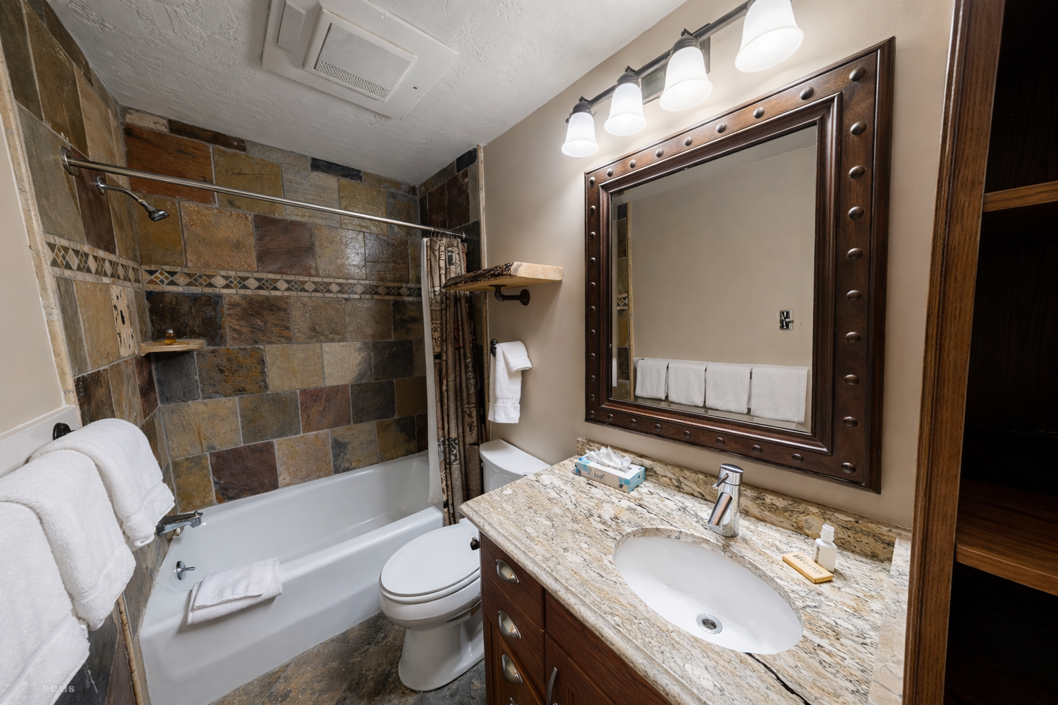 Enjoy the clean shower/tub combo with stylish stone tiles, a spacious vanity, and a large mirror. All set for your stay in Park City.