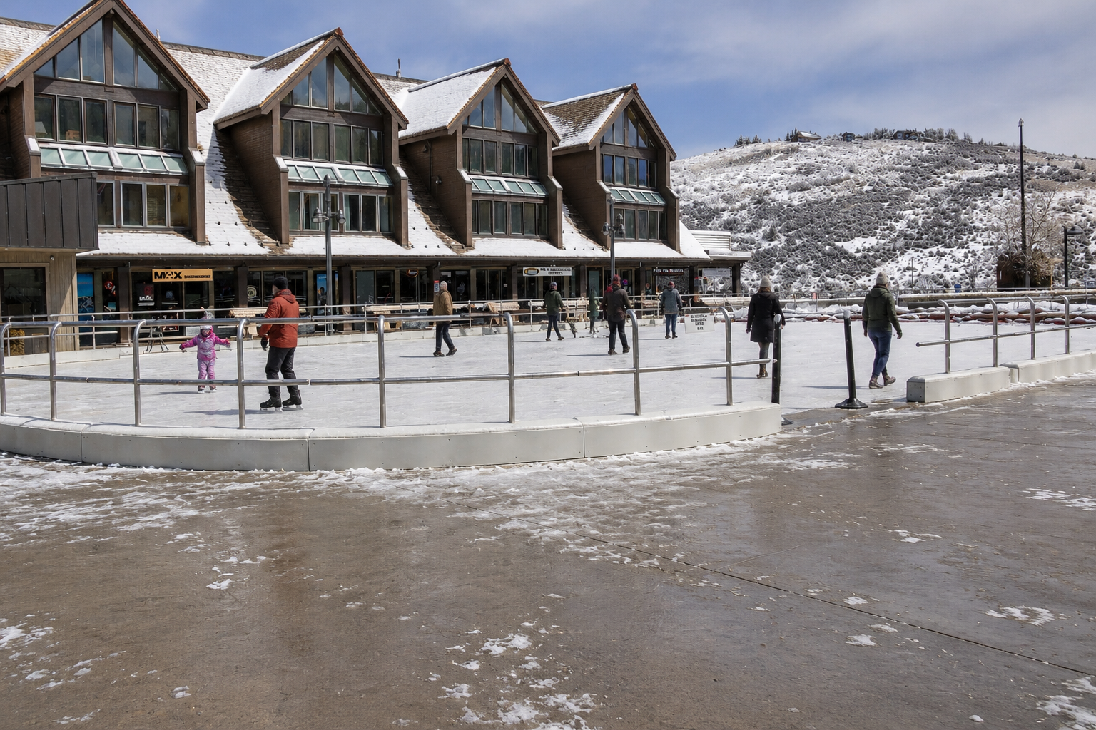 The property is located in a charming mountain village with nearby winter activities, including an outdoor ice skating rink and alpine shops at the base of snow-covered hills.