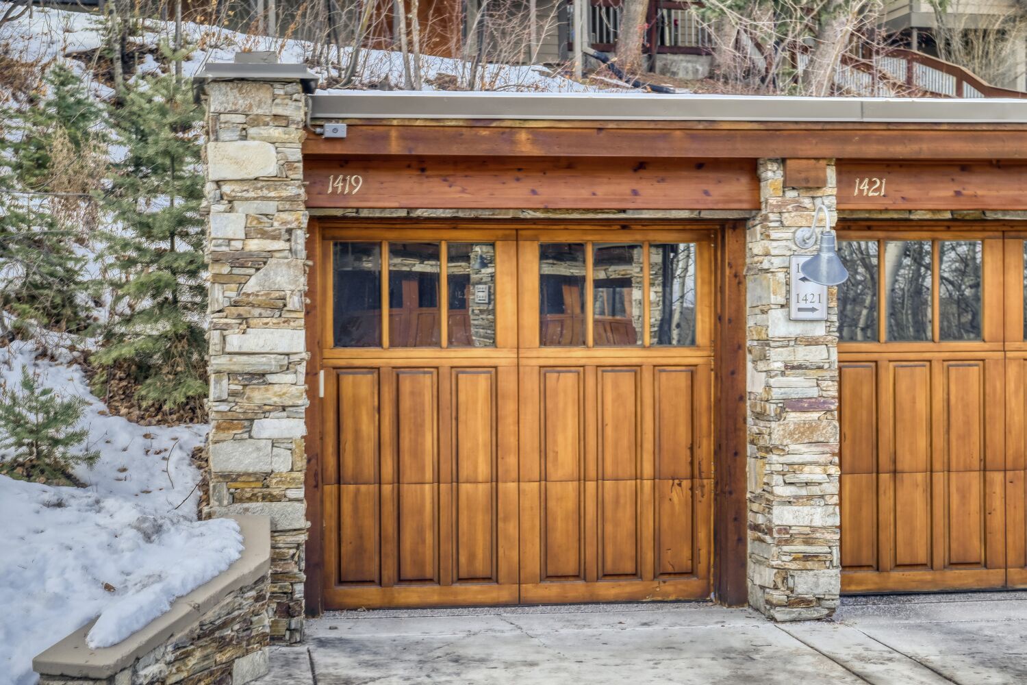 Mountain retreat entrance with rustic stone and timber garage doors, nestled among snowy evergreens for your alpine getaway.