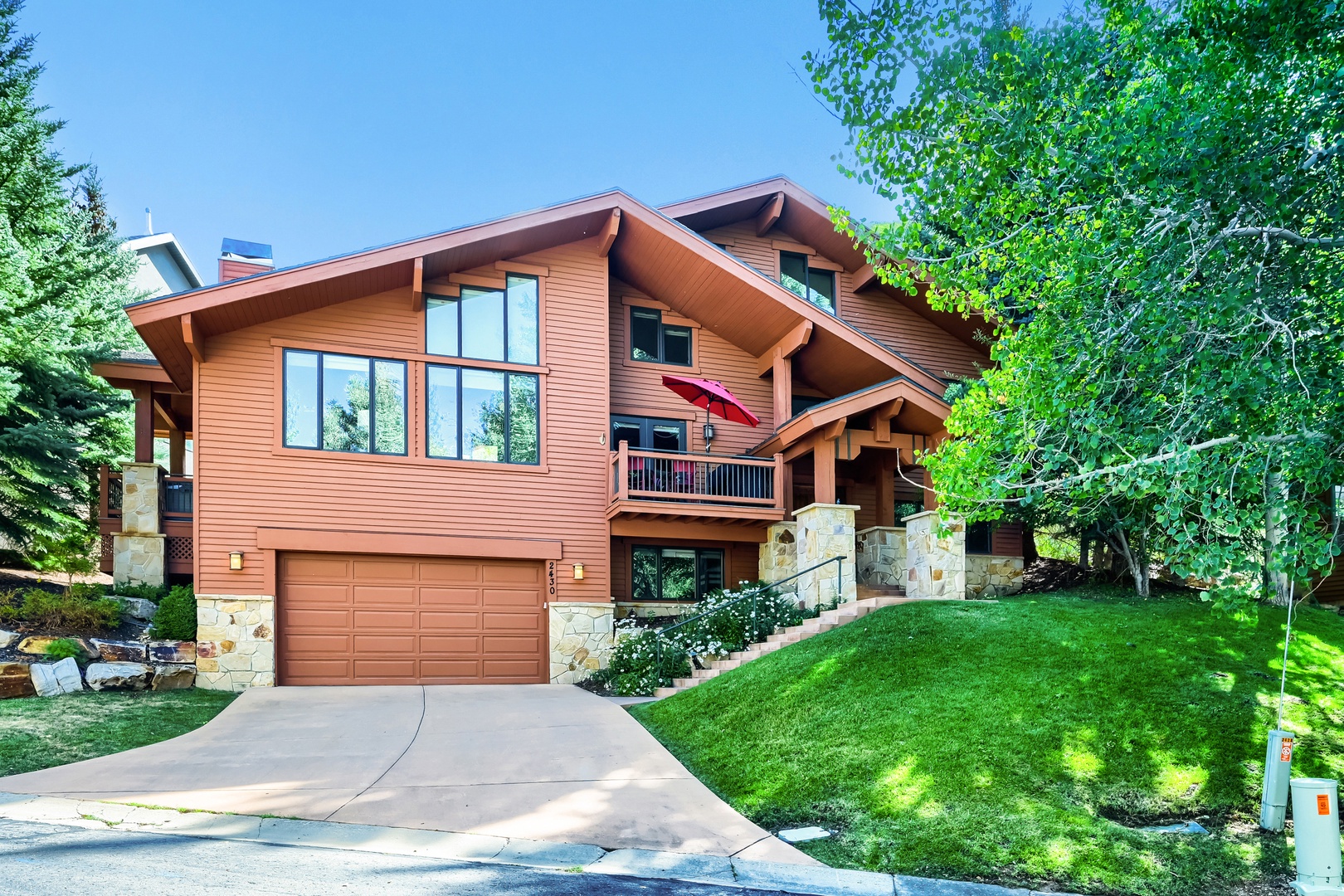 A charming mountain retreat with warm wood siding, expansive windows, and stone accents nestled among tall trees and manicured lawn. Private driveway leads to an inviting multi-level home.