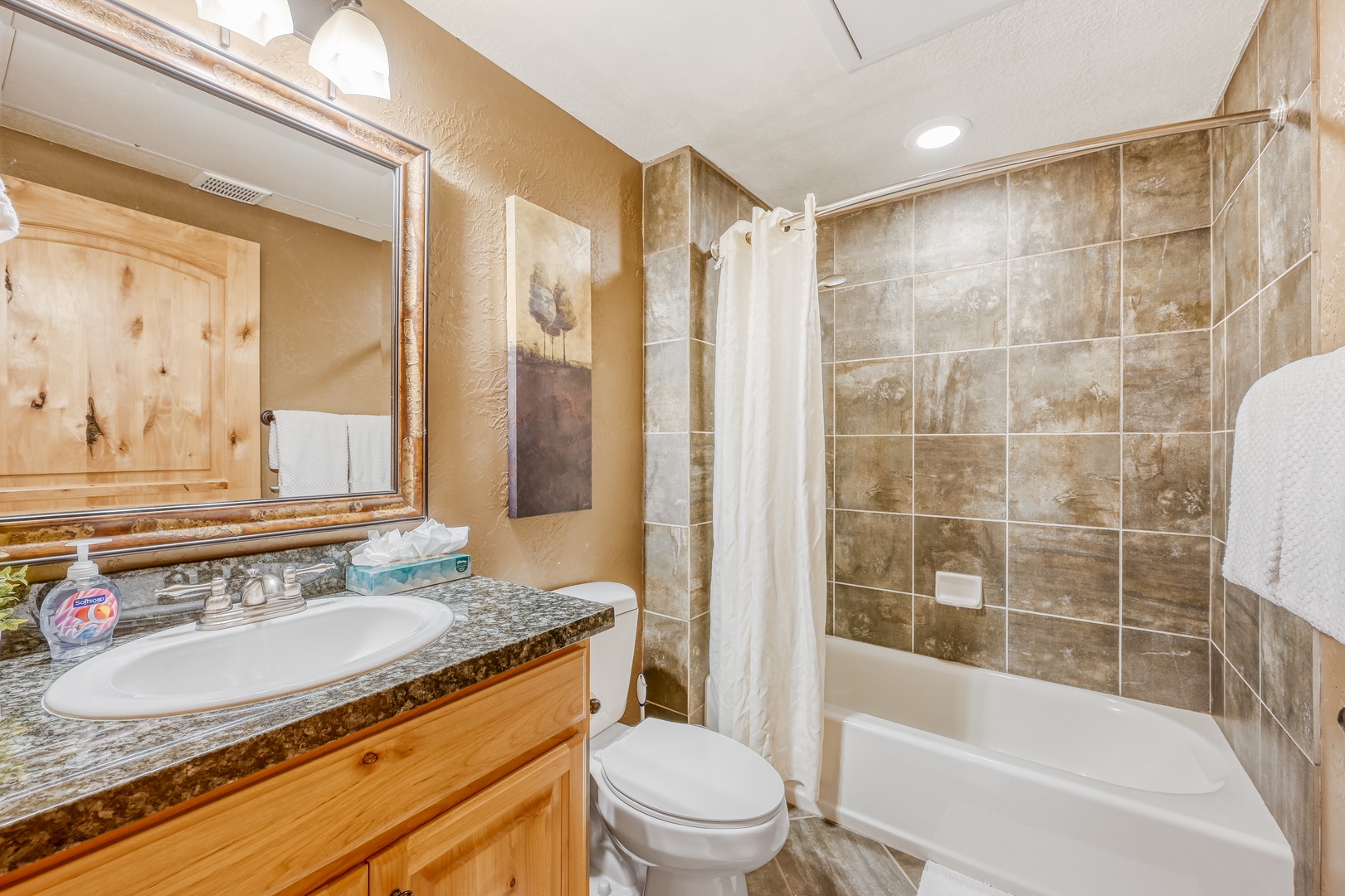 Unwind in your private bathroom featuring granite counters, rustic wood cabinetry, and a relaxing tub-shower combo with elegant tile work.