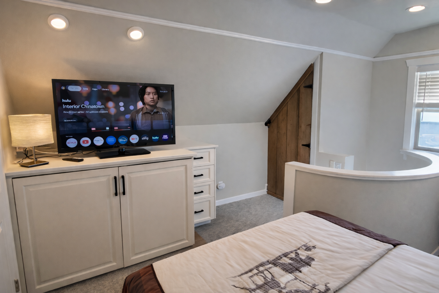 Unwind in the cozy attic bedroom, featuring a large smart TV, dedicated storage, and a comfortable bed under charming sloped ceilings.