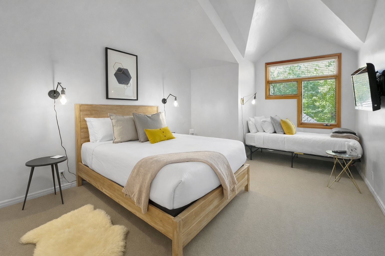 Discover tranquility in this bright, minimalist bedroom featuring a comfortable natural wood bed and a cozy daybed. Large windows offer serene views of the outdoors.