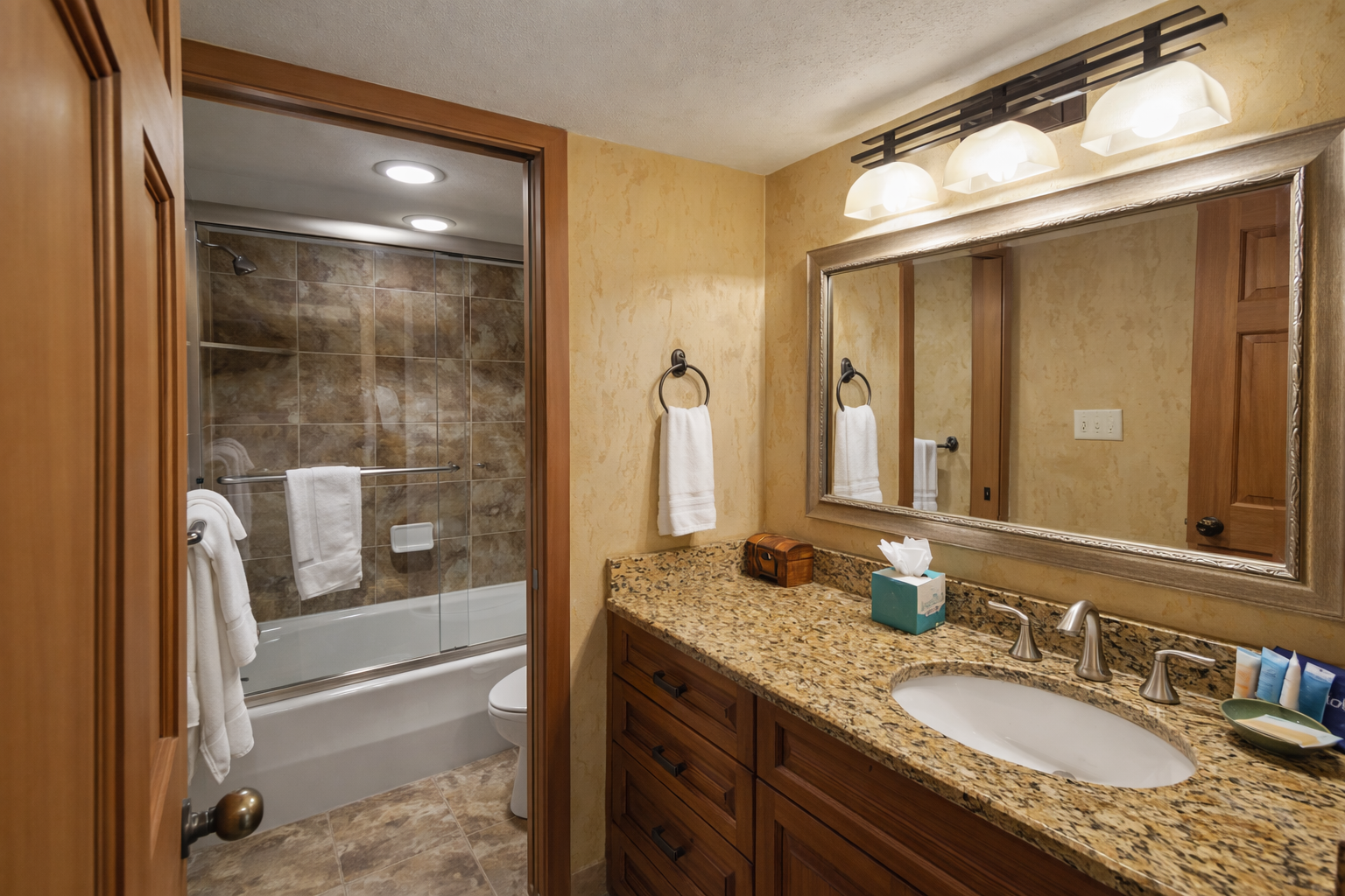 Unwind in your elegant bathroom featuring granite counters, rich wood cabinetry, and a soothing tub-shower combo for relaxing after your adventures.