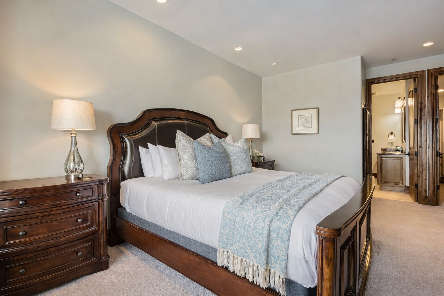 This spacious master suite features a luxurious king bed, soft linens, and a large dresser with a smart TV. Recessed lighting and neutral tones create a bright, tranquil retreat.