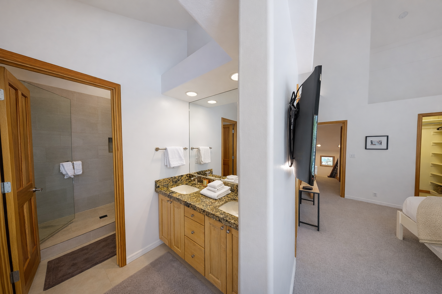 This modern bathroom features a spacious double vanity with elegant granite countertops, a large illuminated mirror, and a sleek, glass-enclosed shower for your convenience.