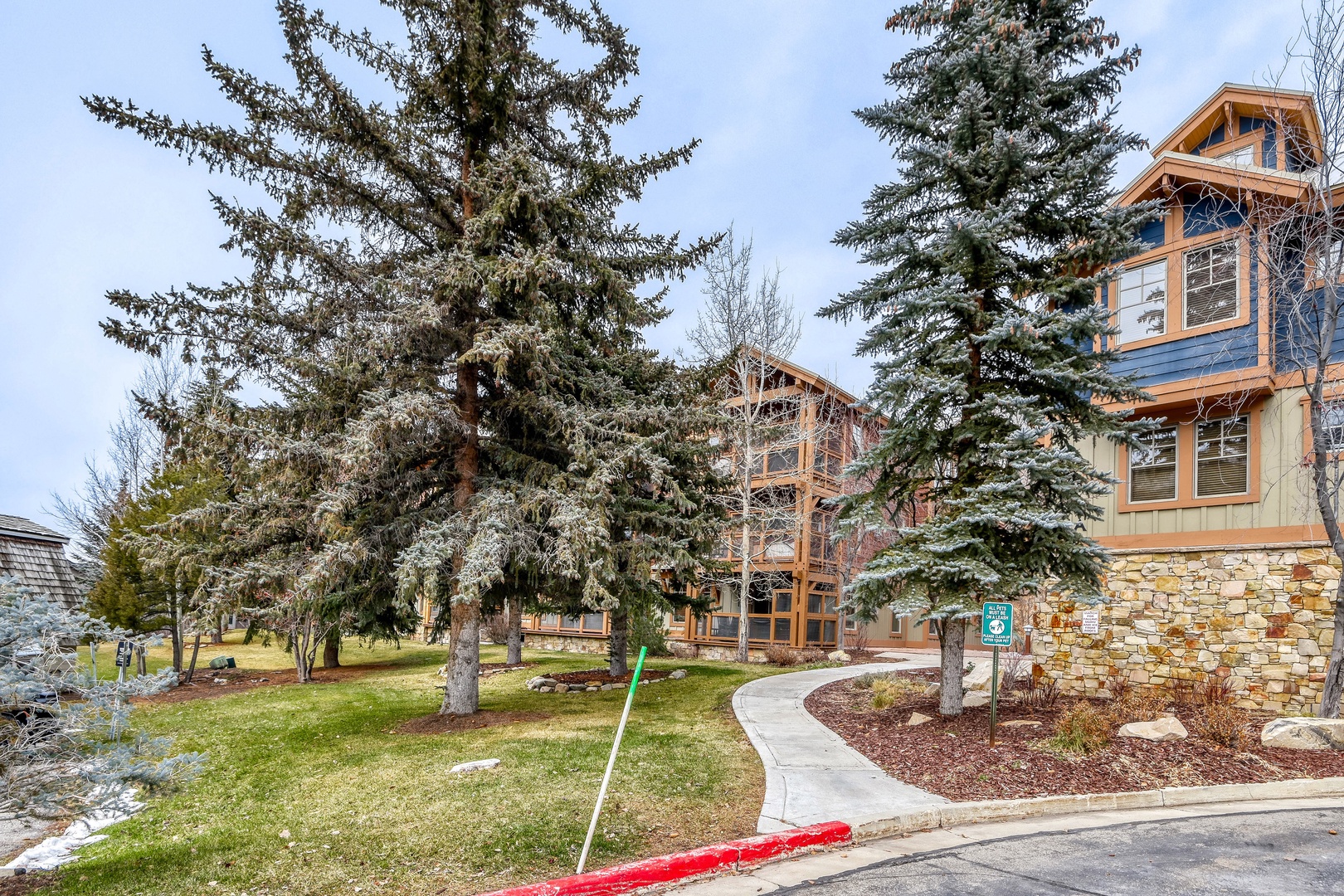 The property sits among tall evergreens in a peaceful mountain setting, with stone-accented architecture and winding walkways that reflect the natural surroundings.