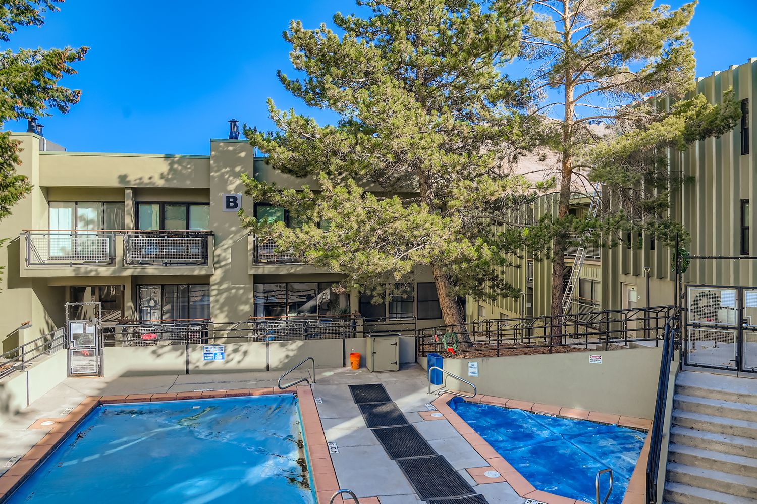 Resort building with outdoor pools surrounded by mature trees under clear blue skies.