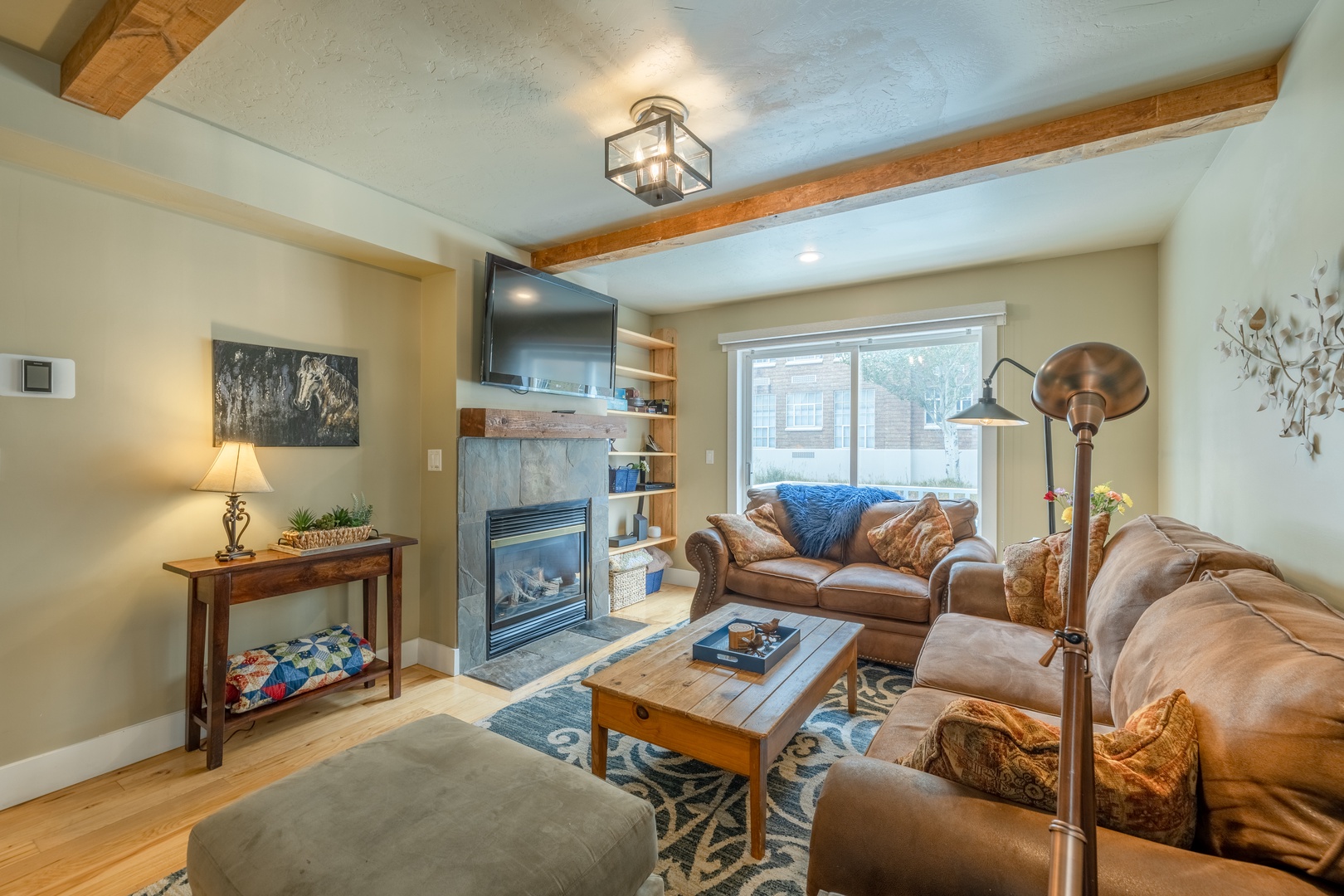 Sink into plush leather sofas in this warm living room with rustic beams overhead, a glowing fireplace, and a large window that fills your retreat with natural light and peaceful views.