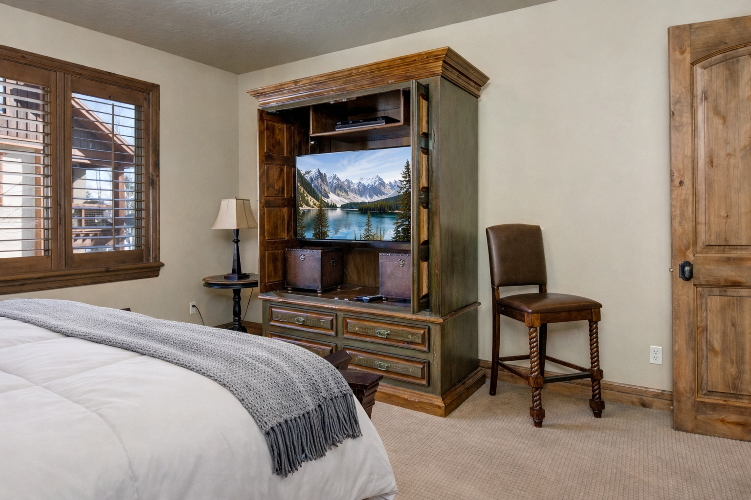 Unwind in this serene primary suite featuring a plush king bed, rich dark wood furnishings, and warm lighting. Large shuttered windows and soft neutral tones create a peaceful mountain sanctuary.