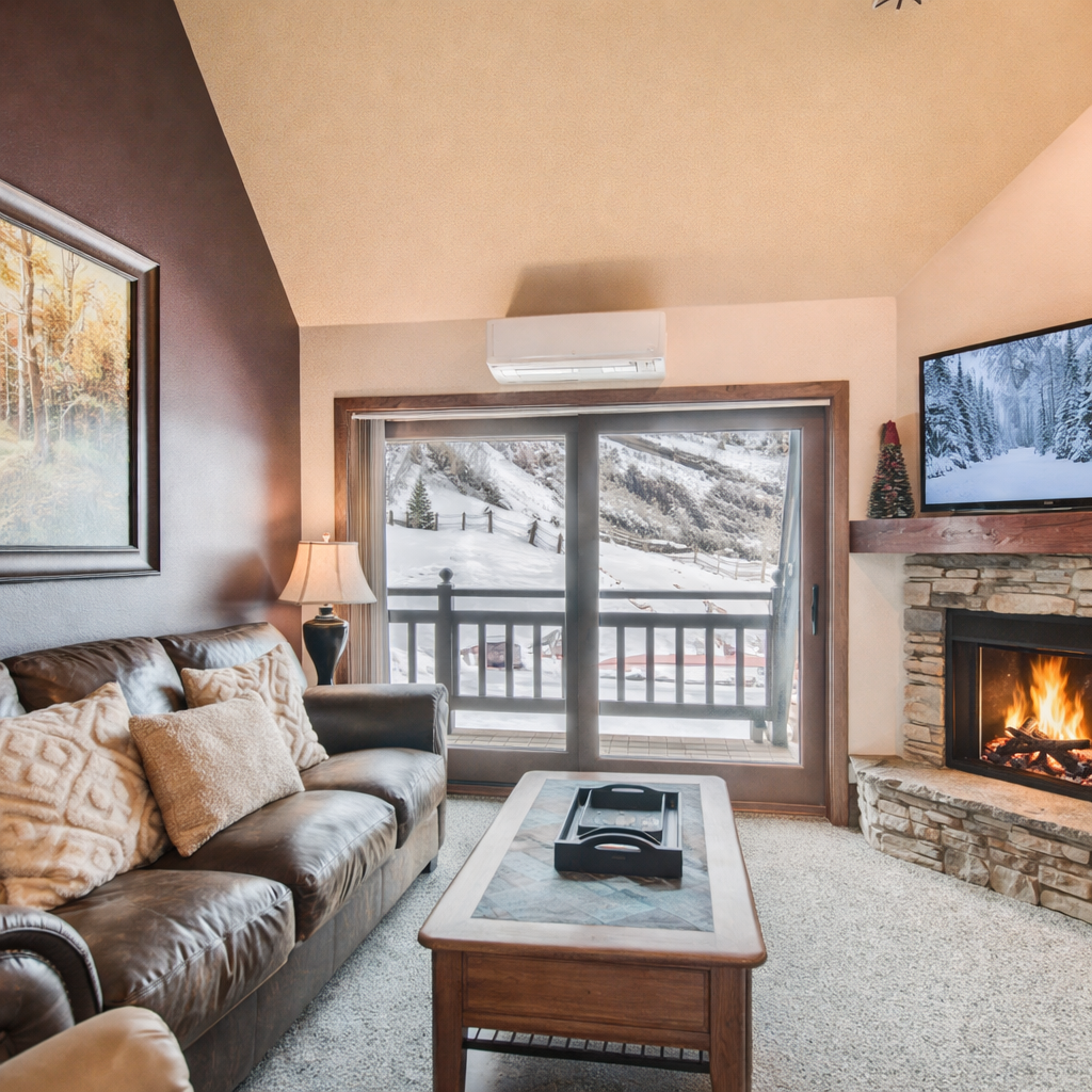 Cozy living room with mountain views, a warm stone fireplace, leather seating, and a smart TV with winter scenery. Perfect for relaxing after skiing, hiking, or exploring Park City. Bright, inviting, and ideal for a comfortable mountain getaway.