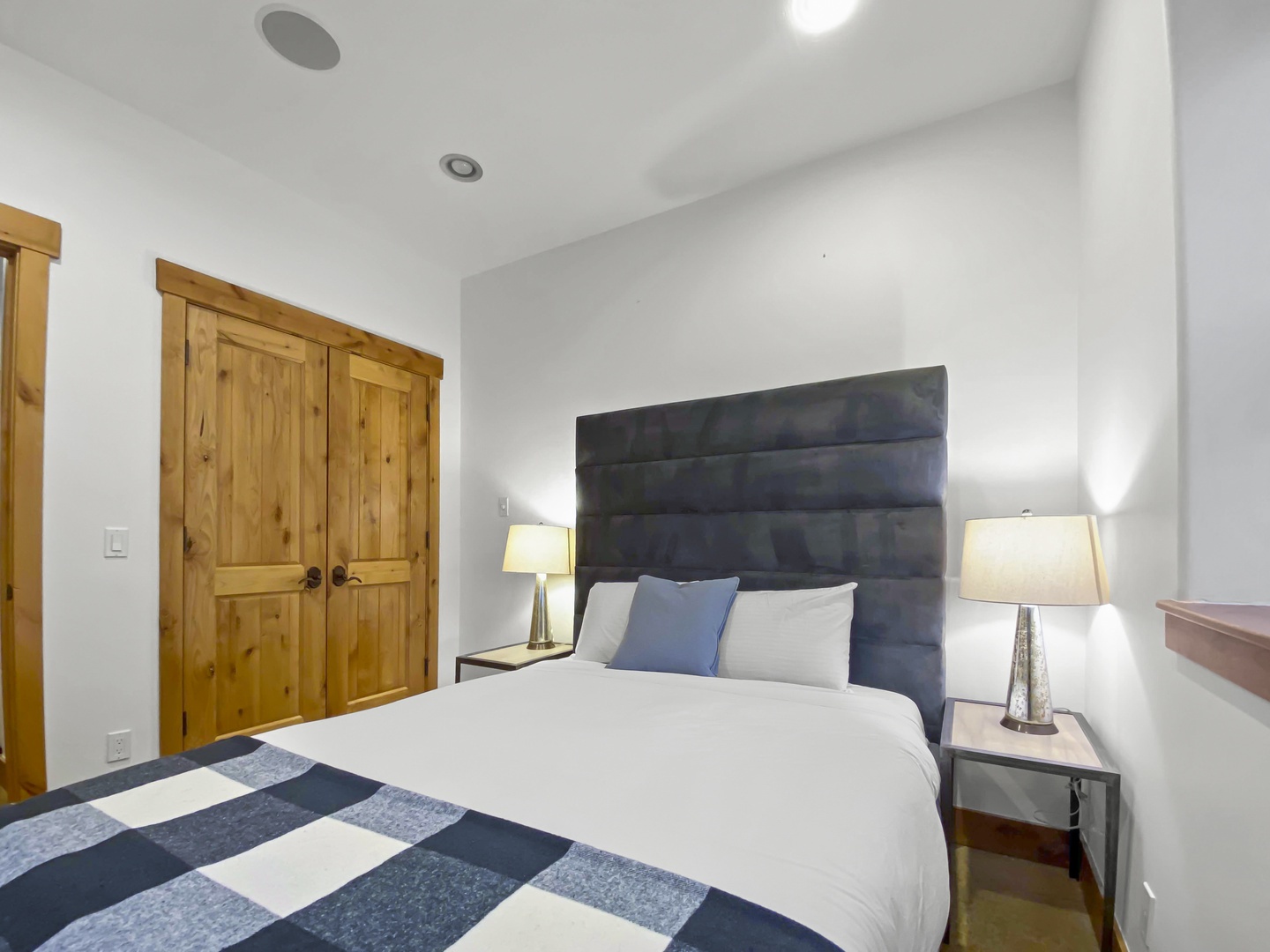 Retreat to this cozy bedroom featuring a plush bed with a stylish blue headboard and warm knotty pine doors. A tranquil space for a restful stay.