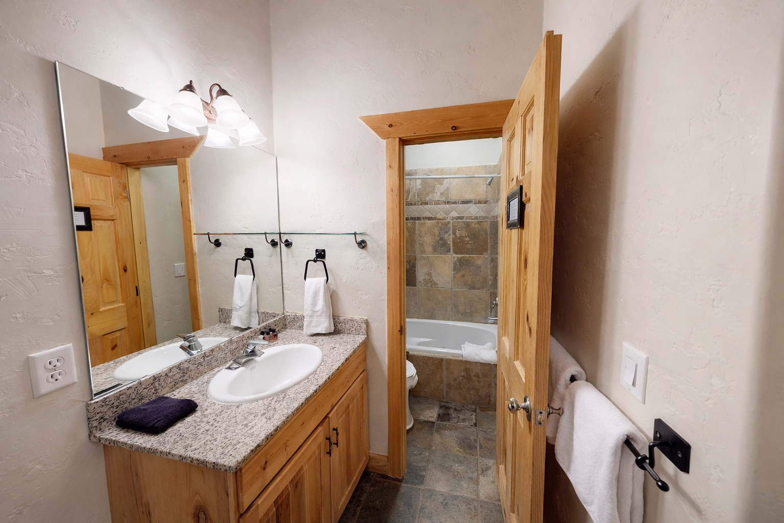 Your private bathroom features warm wood vanity, granite counters, and a relaxing tub-shower combo with natural stone tile.