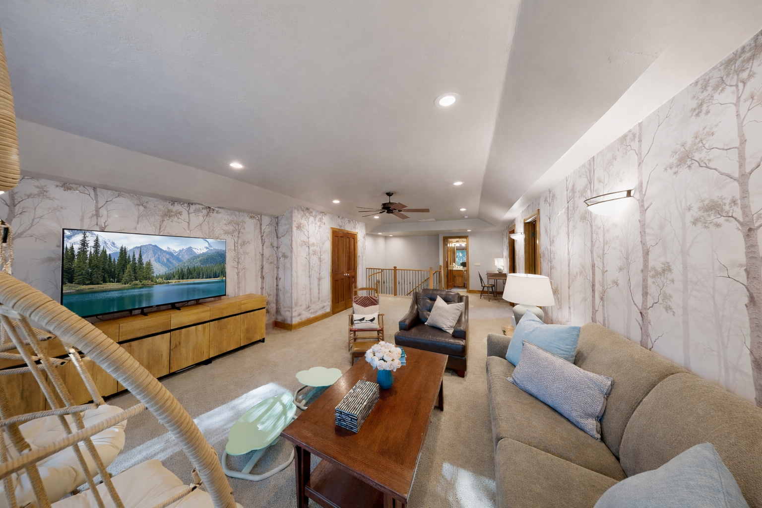 Unwind in your stylish living room with cozy seating, a large TV for movie nights, and elegant tree-patterned wallpaper creating a peaceful retreat.