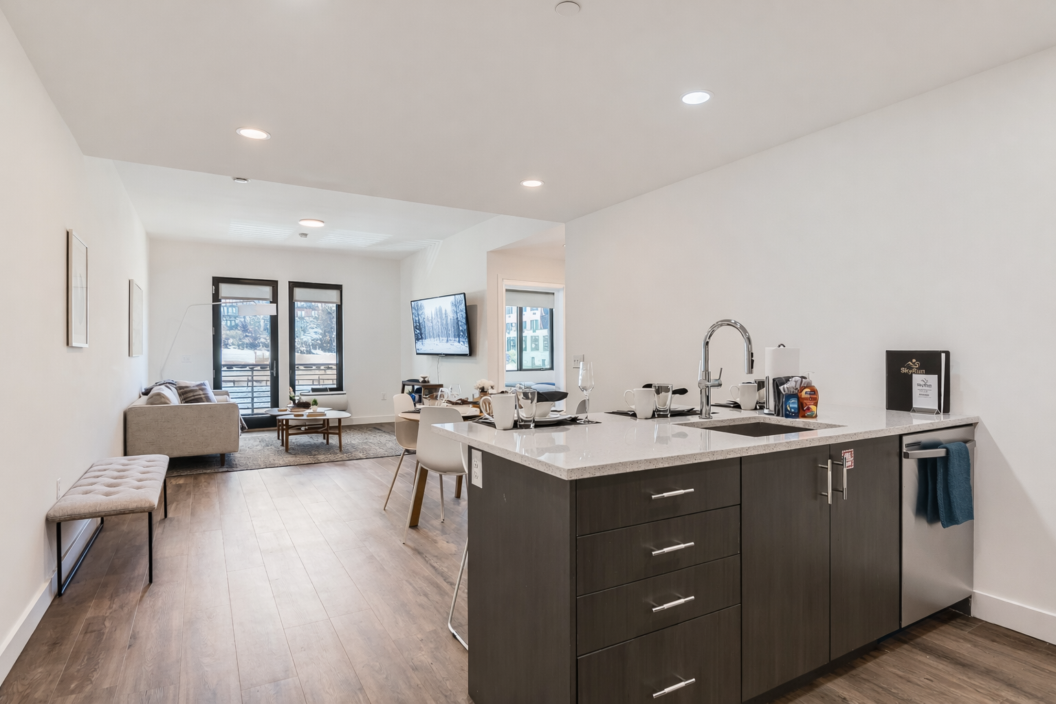 Enjoy this open-concept living area with a dining space for four and a comfortable seating area. The space features modern furniture, wood-look flooring, and large windows with blinds for privacy.