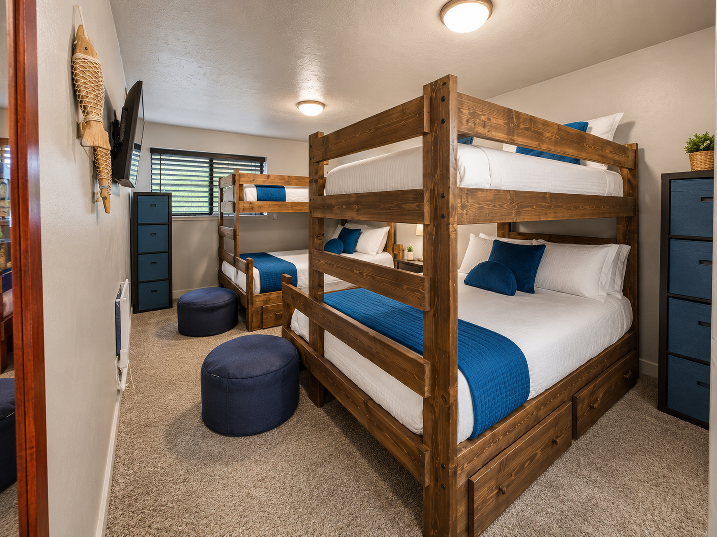 Perfect for families or groups! This custom bunk room features two twin-over-queen wooden beds, a wall-mounted TV, and bright teal accents for a fun and functional stay.