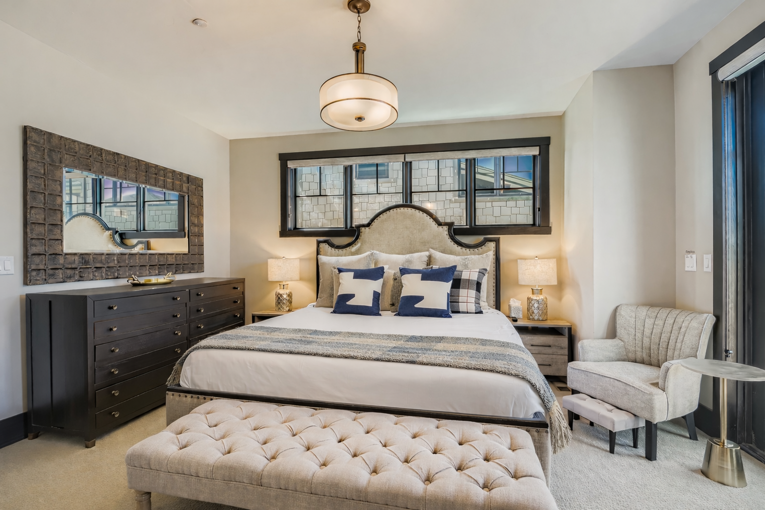 Relax in this bright, sophisticated primary suite featuring a plush king-sized bed, elegant tufted bench, and ample storage. Large windows offer natural light, creating a serene, stylish urban retreat.