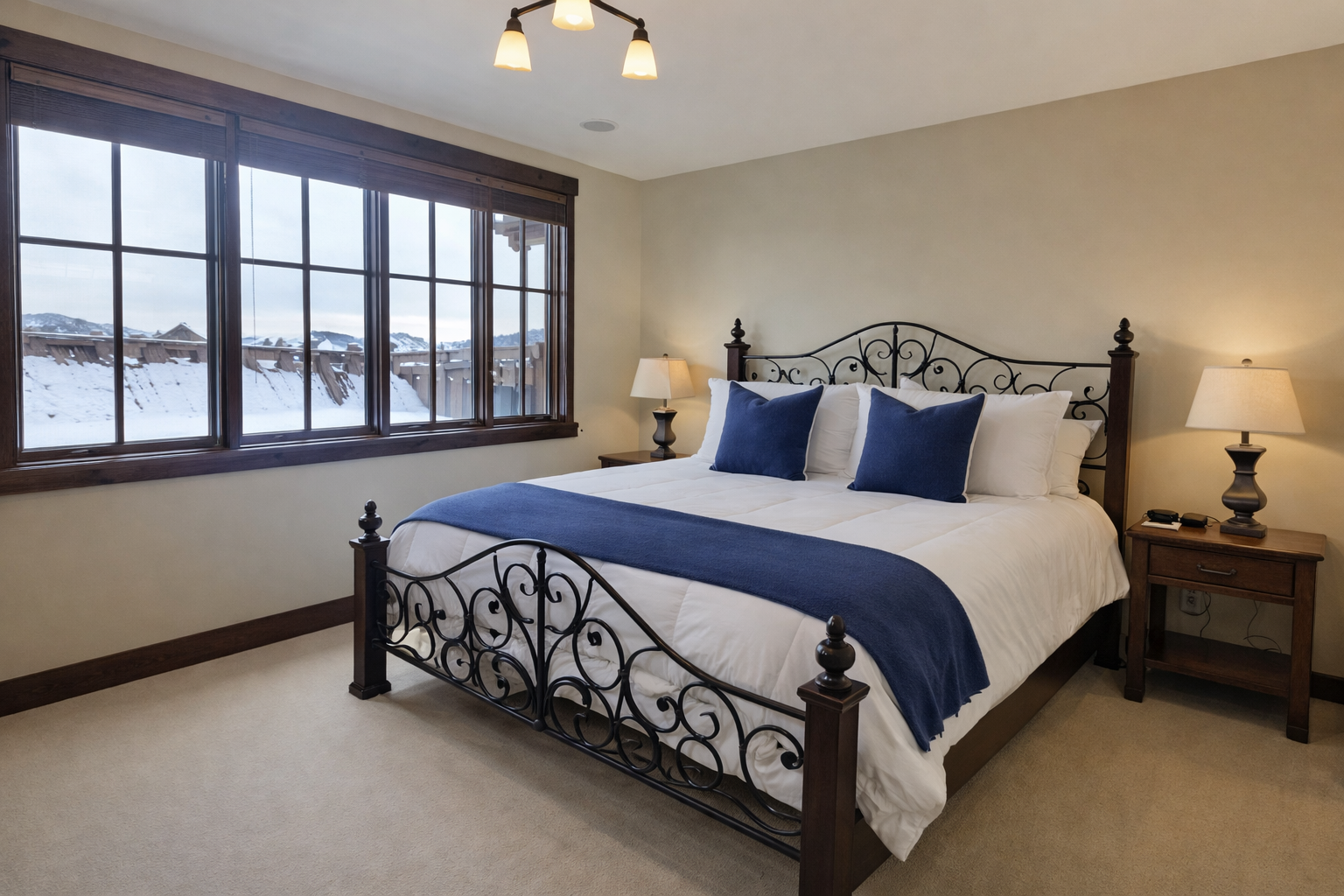 Your cozy bedroom features crisp white linens and elegant blue accents, with stunning winter mountain views through large windows.