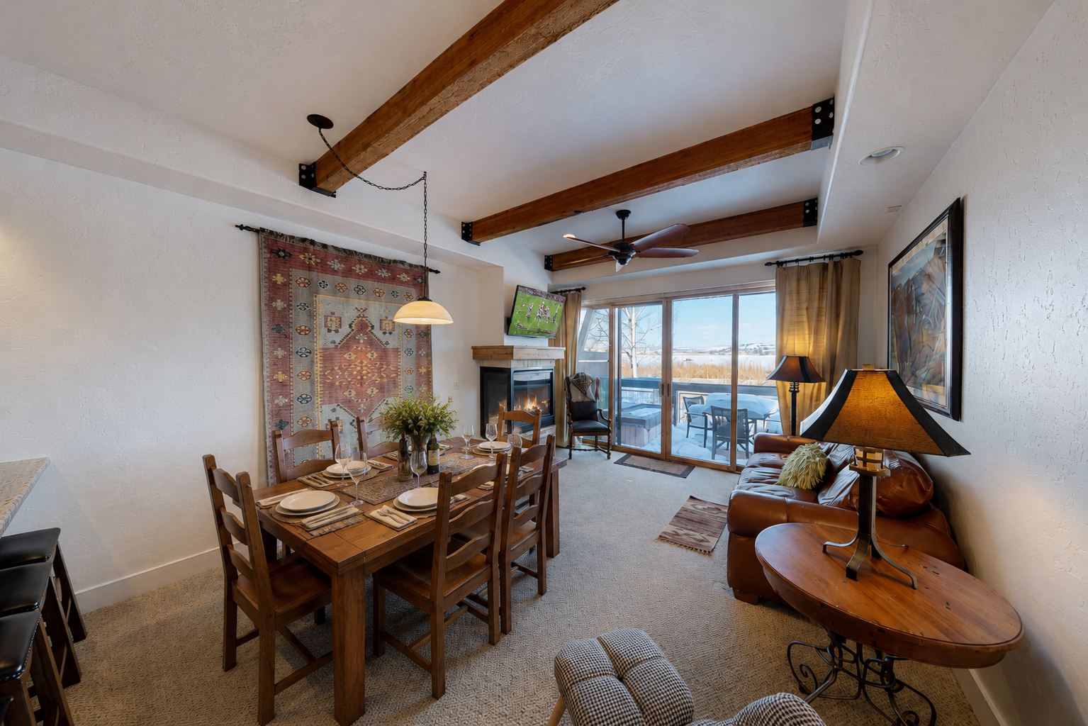 Gather around the rustic dining table under exposed wooden beams, where sunlight streams in through expansive windows. Your cozy retreat features a warm fireplace and opens to a private balcony with stunning views.
