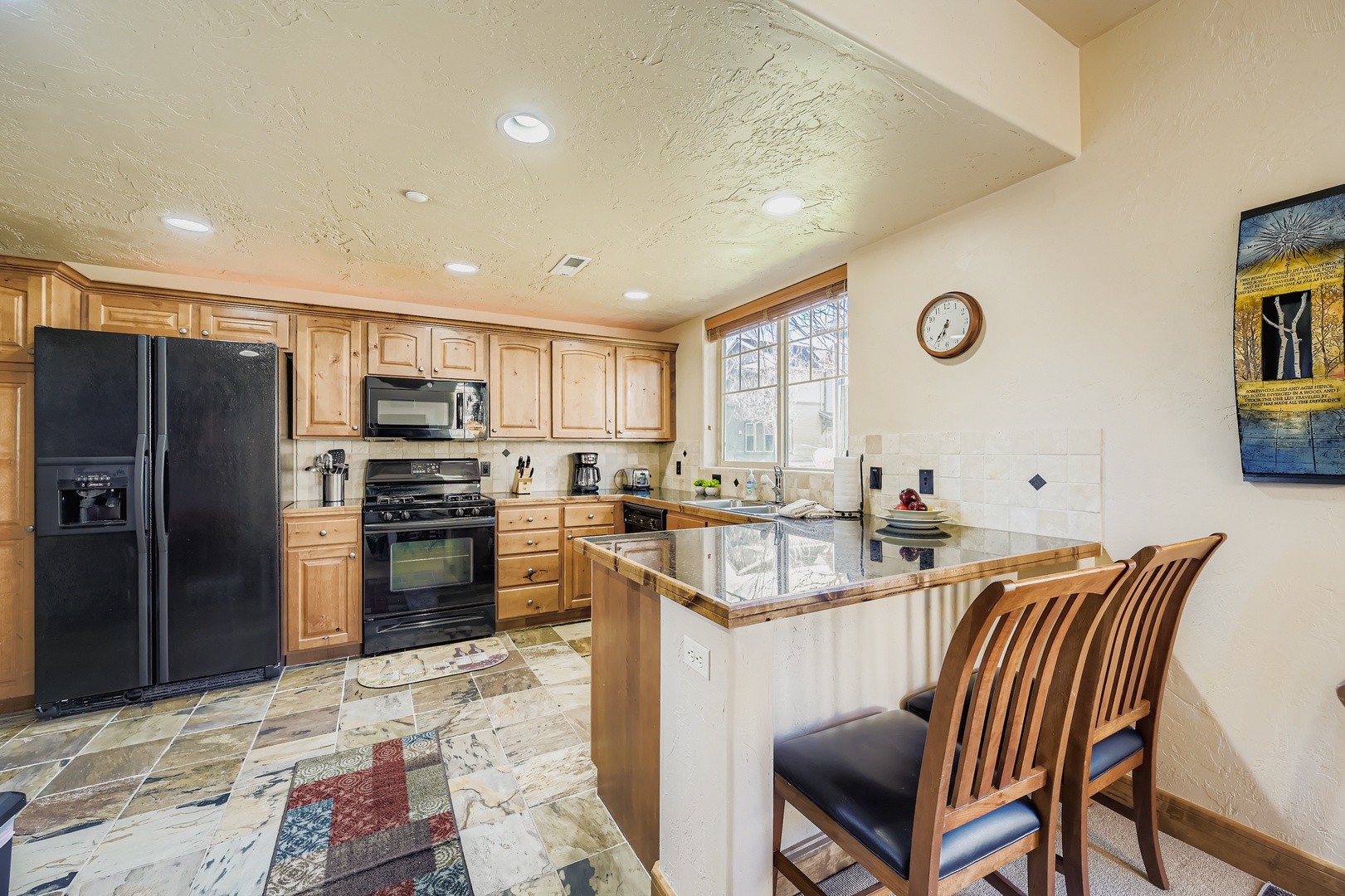 Your fully-equipped kitchen awaits with warm wood cabinetry, granite counters, modern appliances, and an inviting breakfast bar for casual meals and conversation.