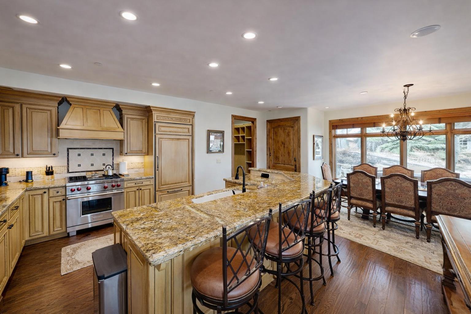 Prepare gourmet meals in this elegant, traditional kitchen. Featuring light wood cabinetry, a grand range hood, and a sprawling granite island, it's a chef's dream with high-end appliances.