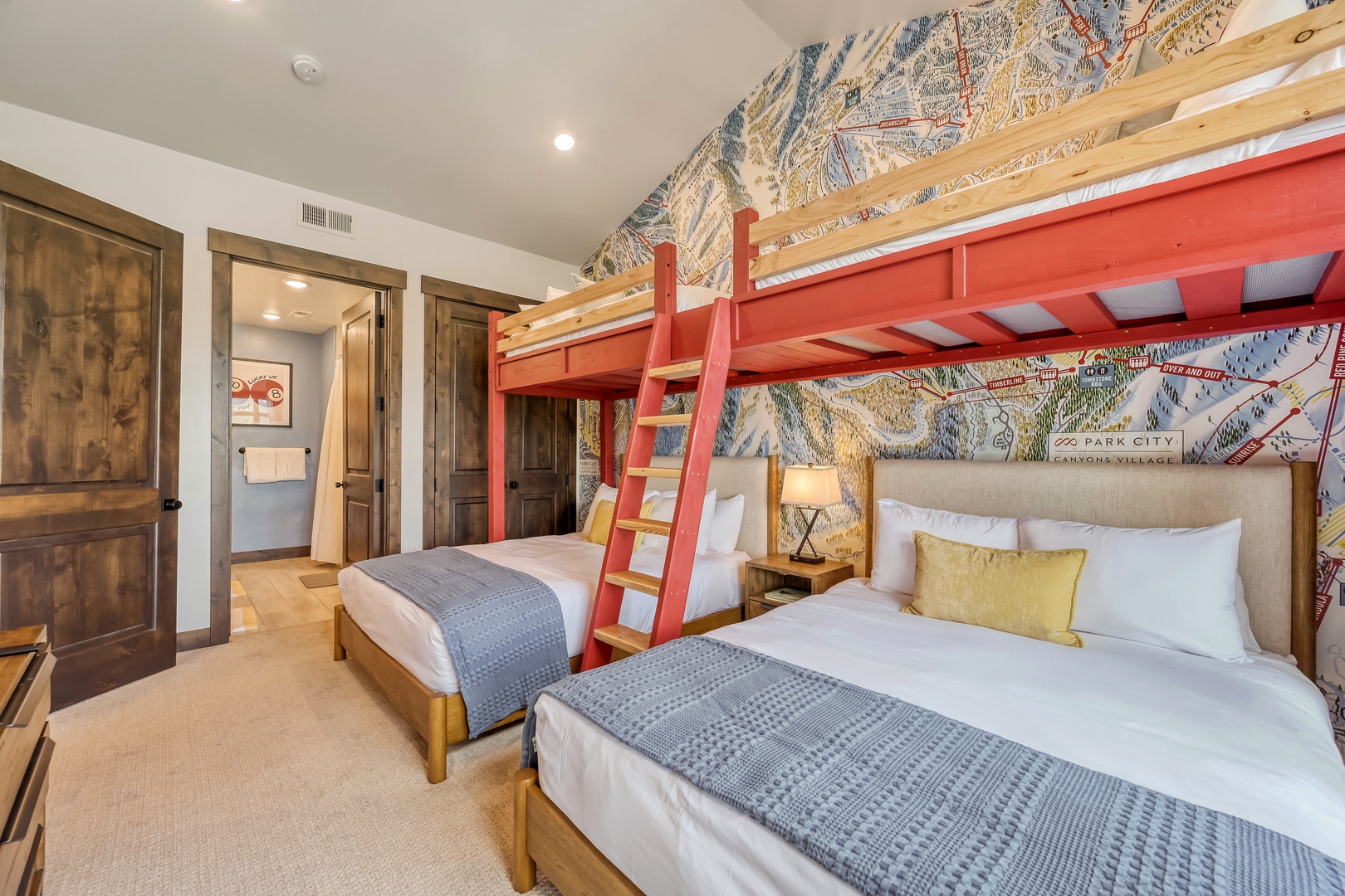 Your mountain retreat features a cozy bedroom with a custom bunk and queen beds, draped in soft linens. A unique ski map accent wall sets the perfect alpine tone for your getaway.