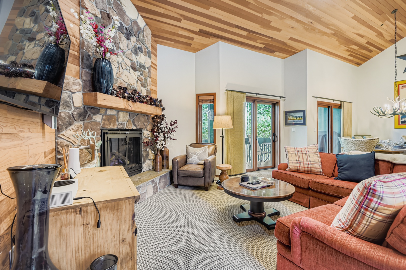 Relax in your spacious living room featuring vaulted wood ceilings, a stunning stone fireplace, and cozy seating that invites you to unwind after a day of mountain adventures.