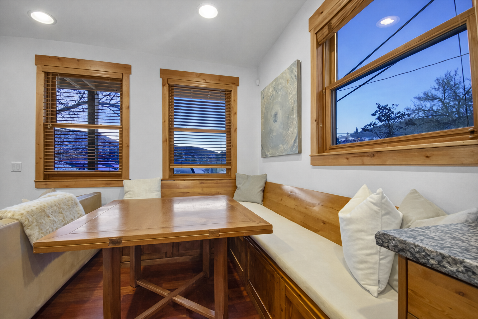 Unwind in your cozy breakfast nook with warm wooden details, plush seating, and evening views through charming windows—perfect for sipping coffee or sharing a quiet meal together.